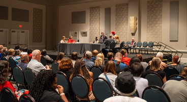 An audience of blind people watch attorneys perform a mock trial on stage.